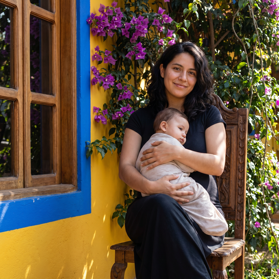 Woman holding a baby in front of a yellow wall with purple flowers